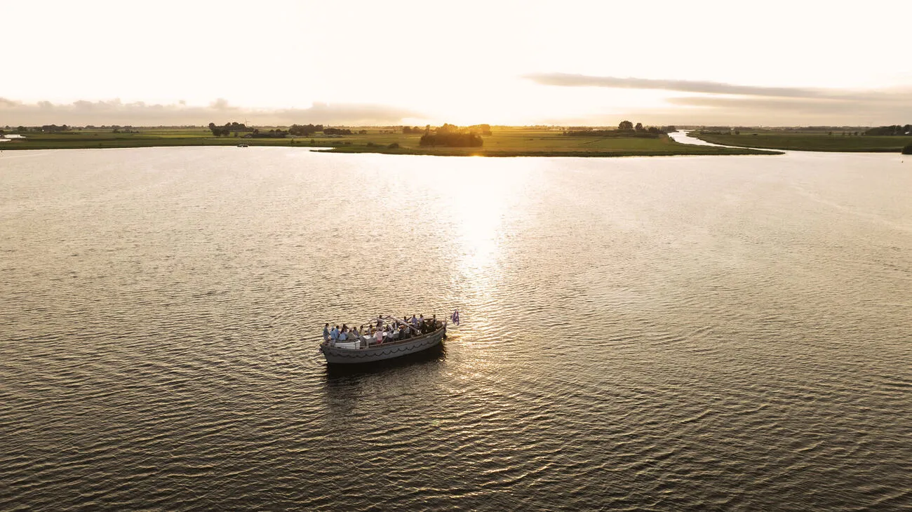 De sloep vaart bij zonsondergang over het weidse Friese water