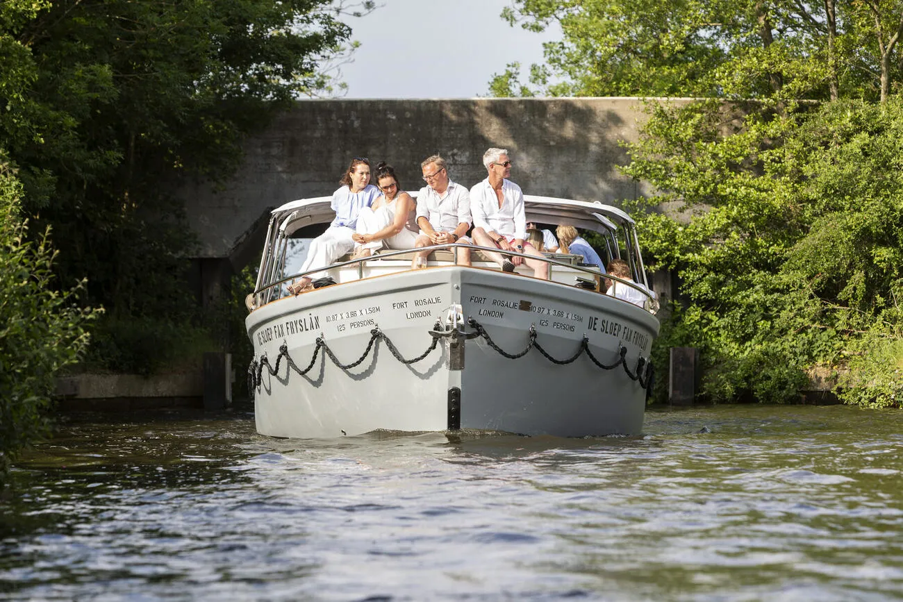 De sloep vaart onder een brug door langs het groen