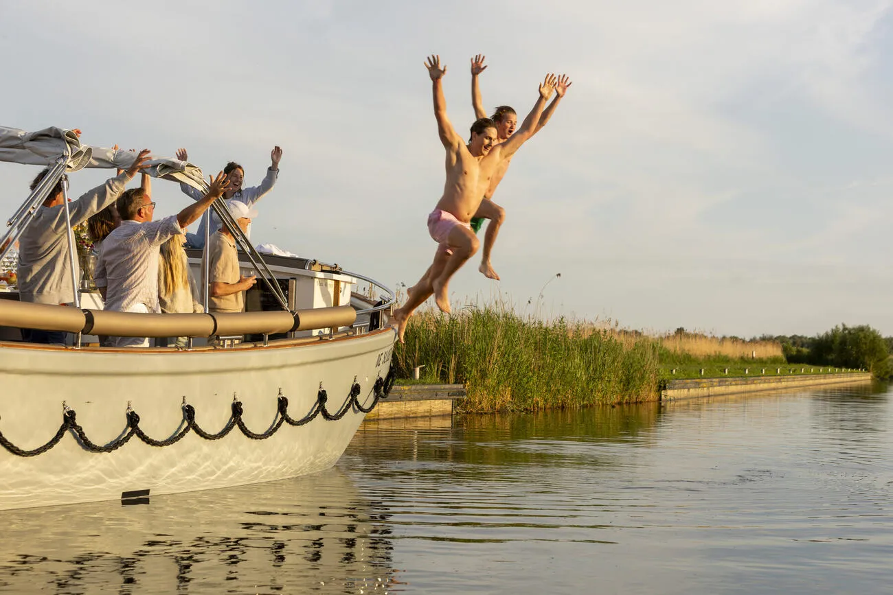 Twee gasten springen lachend van de sloep het water in
